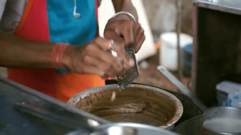 Shantanu's hands grating ginger into a kadhai of bubbling chai